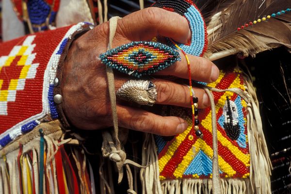 Beaded Native American jewelry and fringe clothing with a hand holding beadwork in a colorful pattern