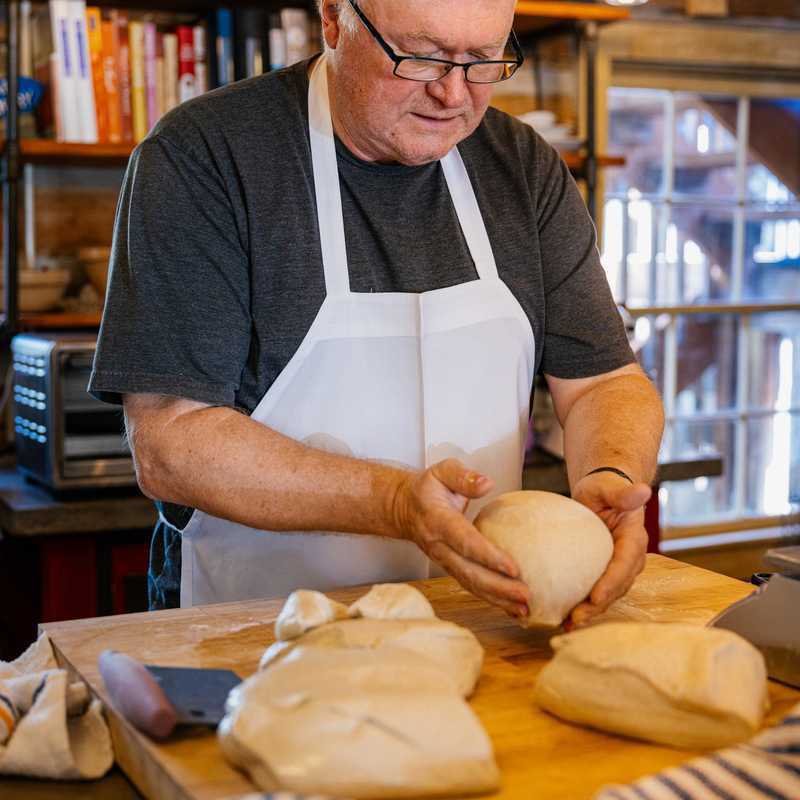 Baker kneading dough on a counter in a bakery workshop with pastries and ingredients nearby