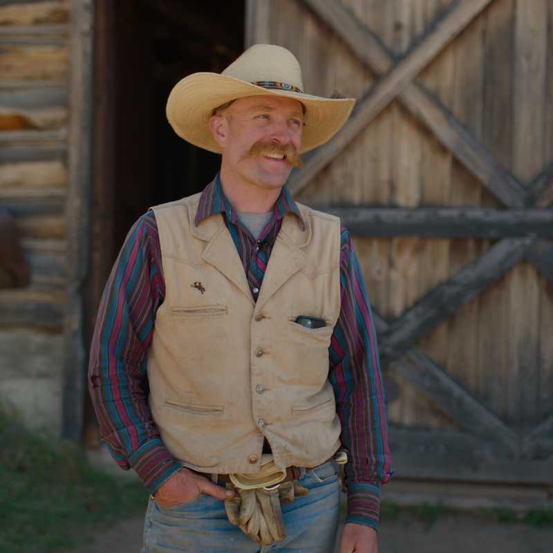 Man in cowboy hat standing in front of a wooden barn in Montana at sunset