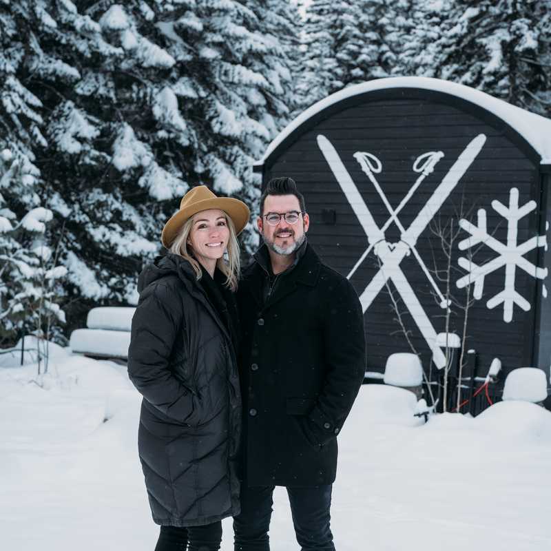 Couple standing in snowy landscape in front of a black winter-themed metal shed in Montana