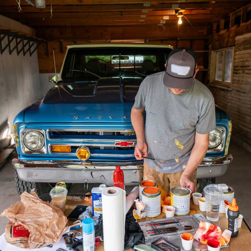Person preparing a table of supplies in a garage in front of a parked blue classic pickup truck with Montana-style tourism appeal