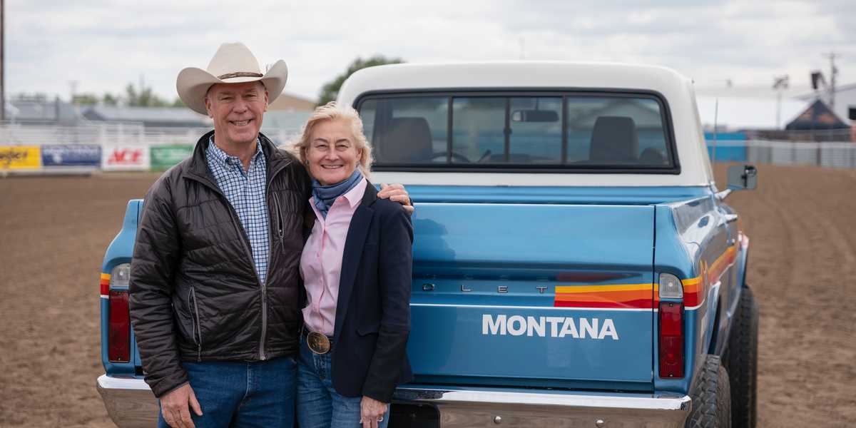 Two people posing with a Montana-branded blue pickup truck outdoors at an event in Montana