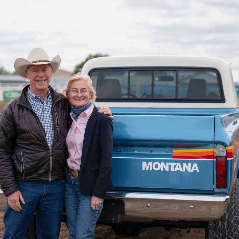 Two people posing with a Montana-branded blue pickup truck outdoors at an event in Montana
