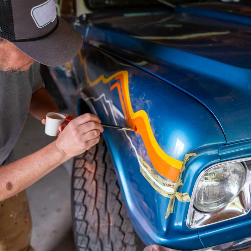 Auto body repair in progress on a blue vehicle, with a worker applying heat or light to a damaged front panel