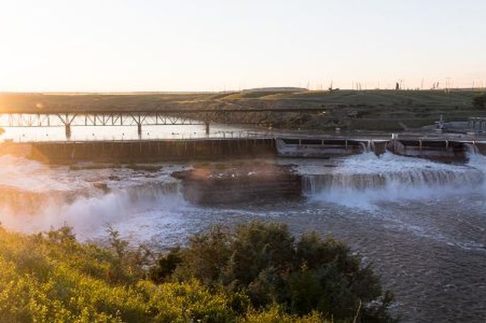 Sunset over a Montana bridge spanning a wide river with mist rising from the water and nearby riverbanks and hills