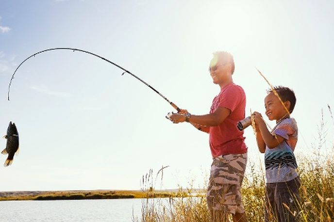 Two people fishing by the shore in a Montana lake with tall grass and a large fish catch in view