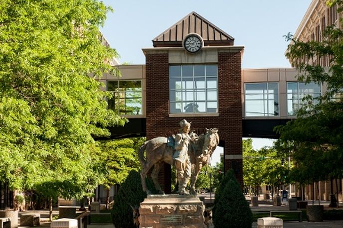 Outdoor view of a campus building with a large bronze statue and landscaping trees in front