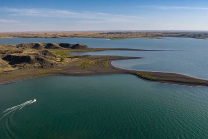 Aerial view of a Montana river with a curved shoreline and surrounding dry hills under clear skies