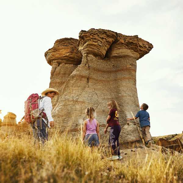 Group of people hiking near a large, unique rock formation during sunset, with a mix of adults and children exploring the area.