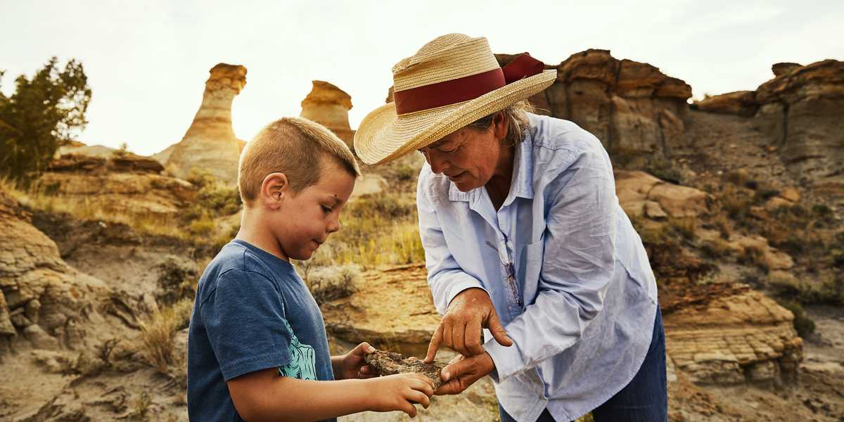 Adult helping a child with a small object outdoors at a rocky Montana landscape during sunset