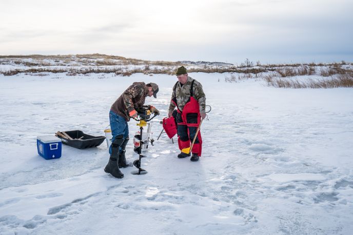 Two fisherman drilling an ice fishing hole.