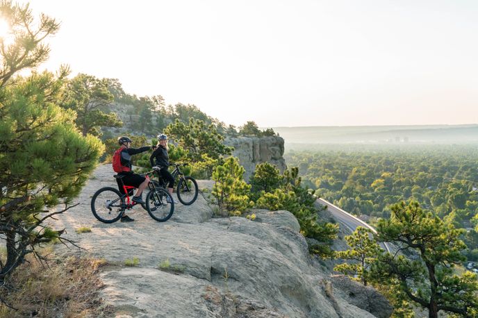 Two cyclists on mountain bikes pause on the rims, overlooking the city of Billings.
