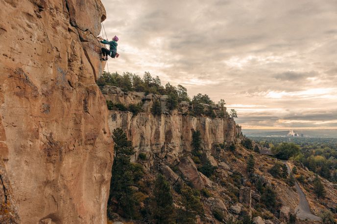 Rock climber ascending a steep cliff face with a scenic view of the city of Billings.