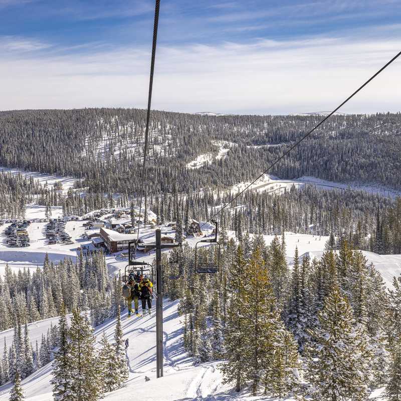 Ski resort hillside with snow-covered trails, lodge buildings, and forested slopes in Montana