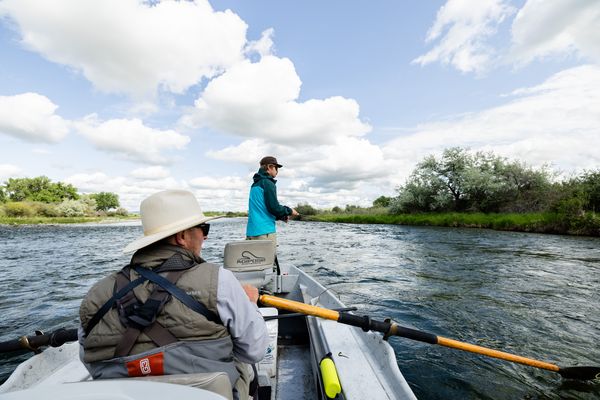 Two anglers on a canoe traveling on a river through Montana’s countryside