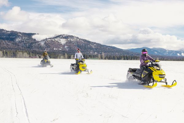 Snowmobiles ride across a snowy Montana landscape with mountains in the background