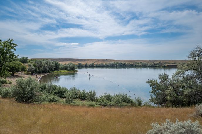 Calm river with a small dock and paddleboat near the shoreline in Montana under a partly cloudy sky