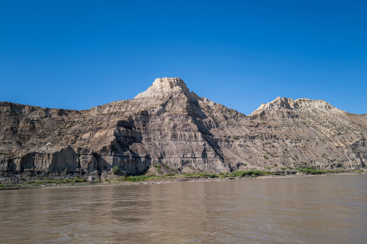 Rocky mountain cliffs rising above a river under a clear blue sky in Montana