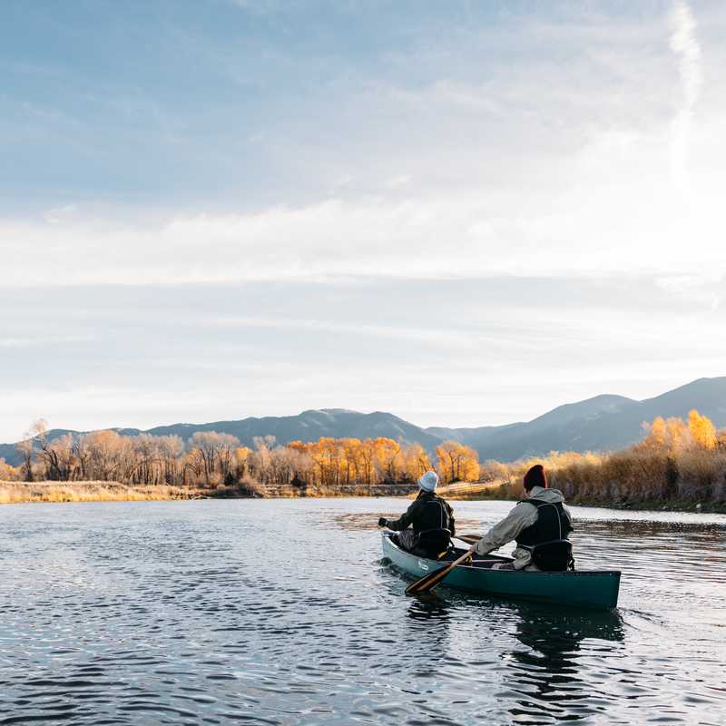 Canoe on a calm Montana river at sunset with mountains and autumn trees in the background