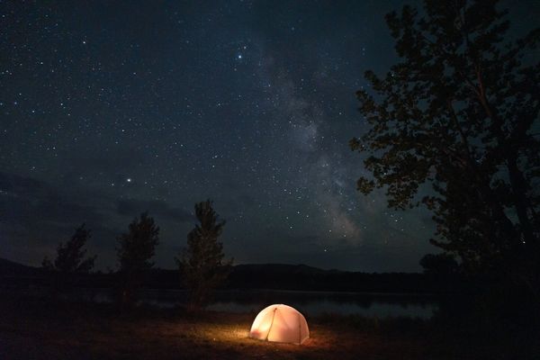 Camping tent glowing at night under a starry sky by a lakeshore in Montana