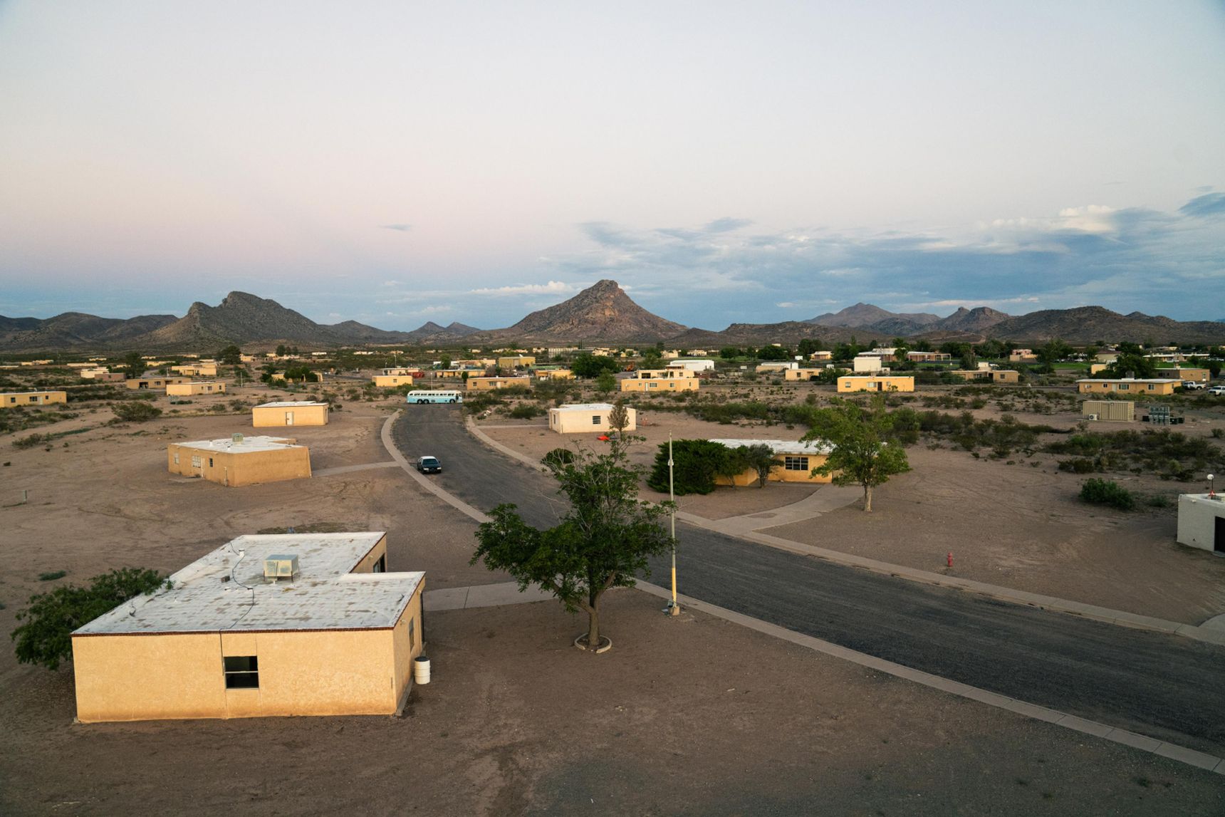 Aerial view of a desert town with scattered houses and a winding road, surrounded by a landscape and distant mountain.