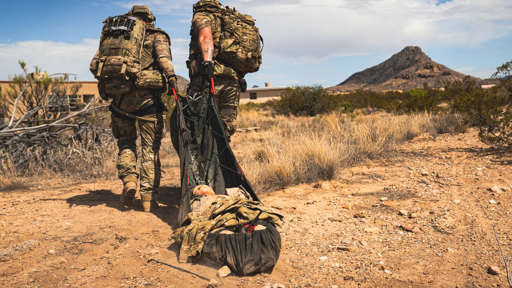 Image of 2 men carrying a wounded soldier in the form of a fake doll.
