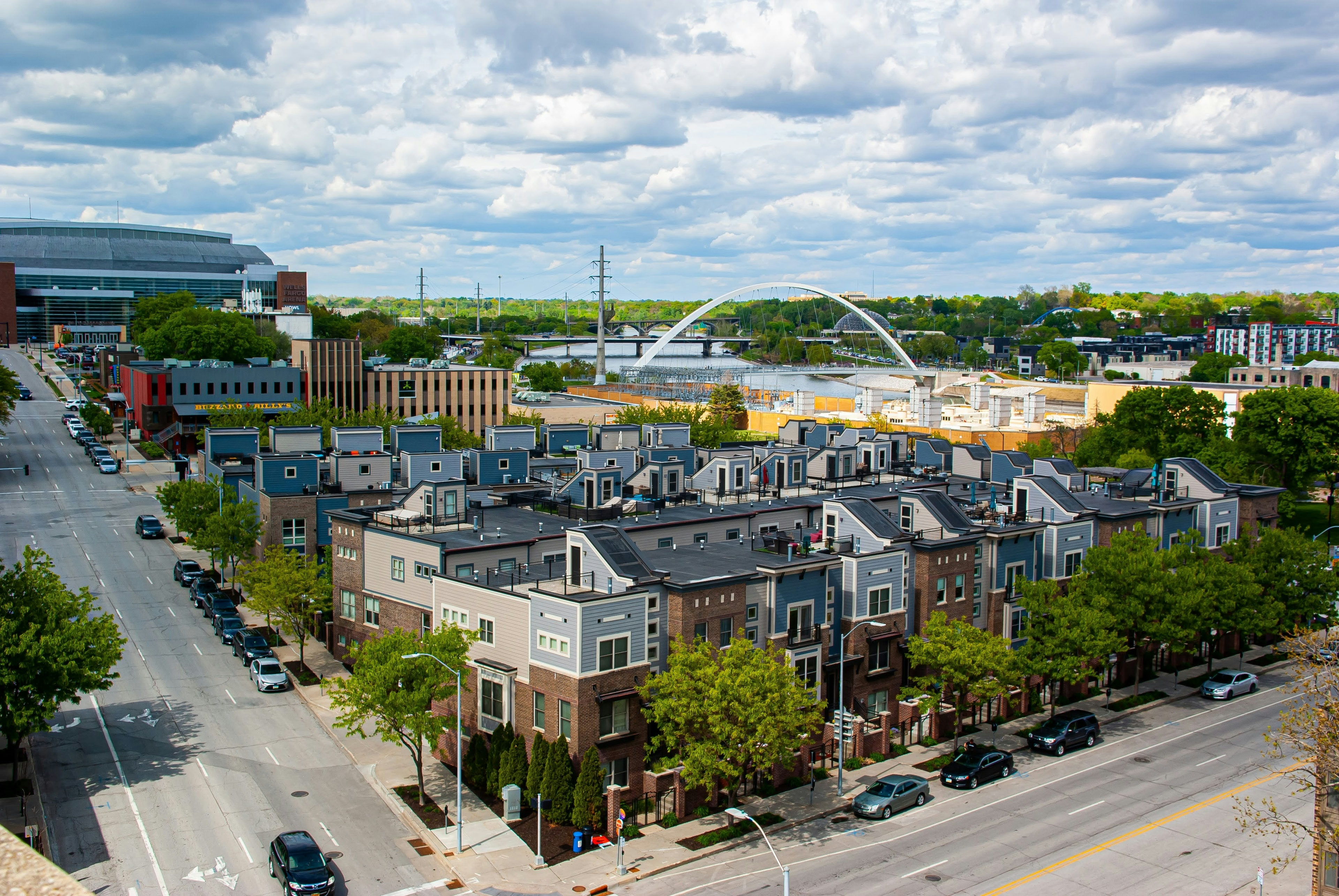 The cityscape of Des Moines, Iowa, featuring modern townhouses, tree-lined streets, and a cloudy sky.