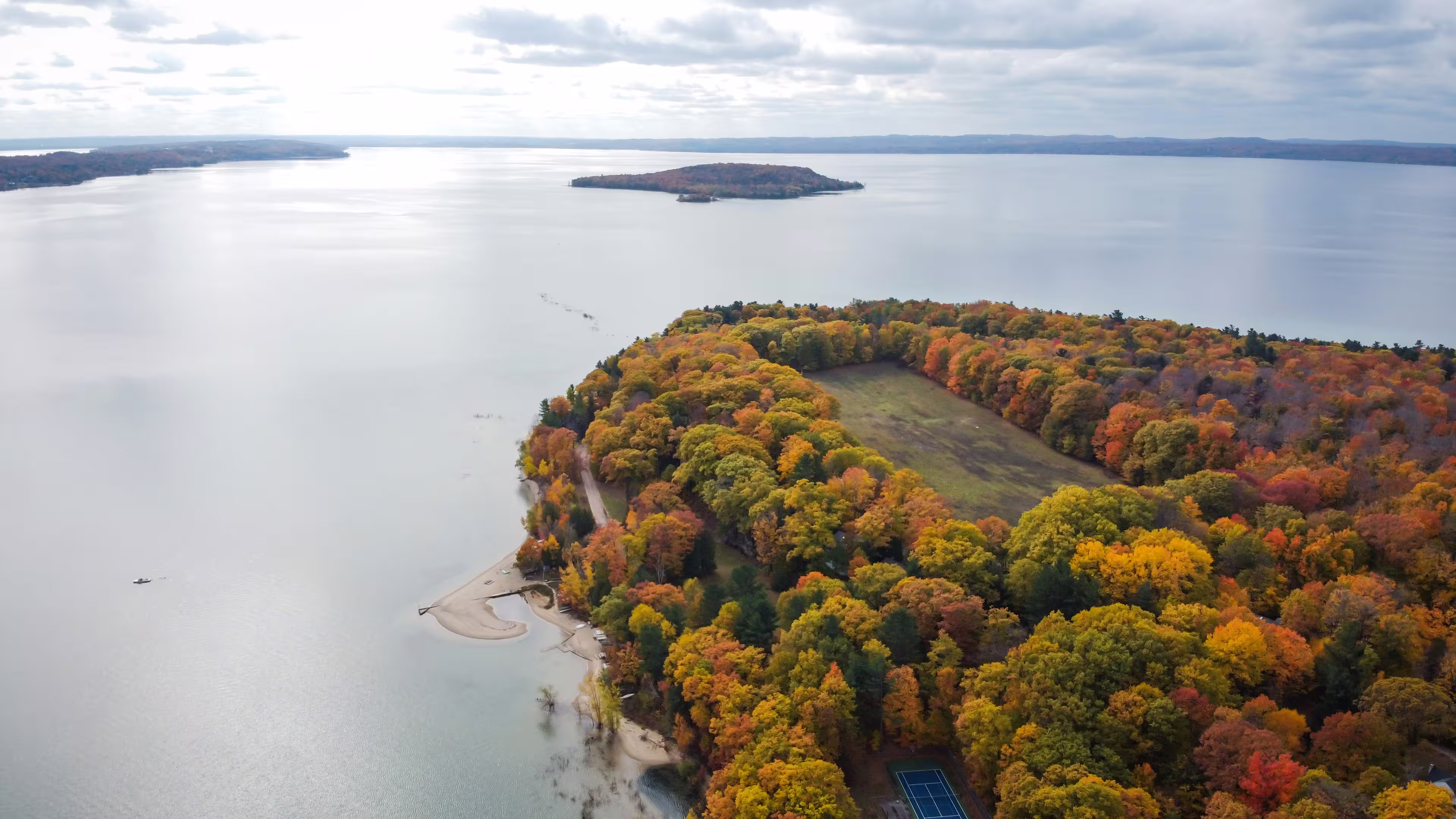 Aerial view of Traverse City, Michigan, with autumn trees, surrounded by a calm lake under a cloudy sky.