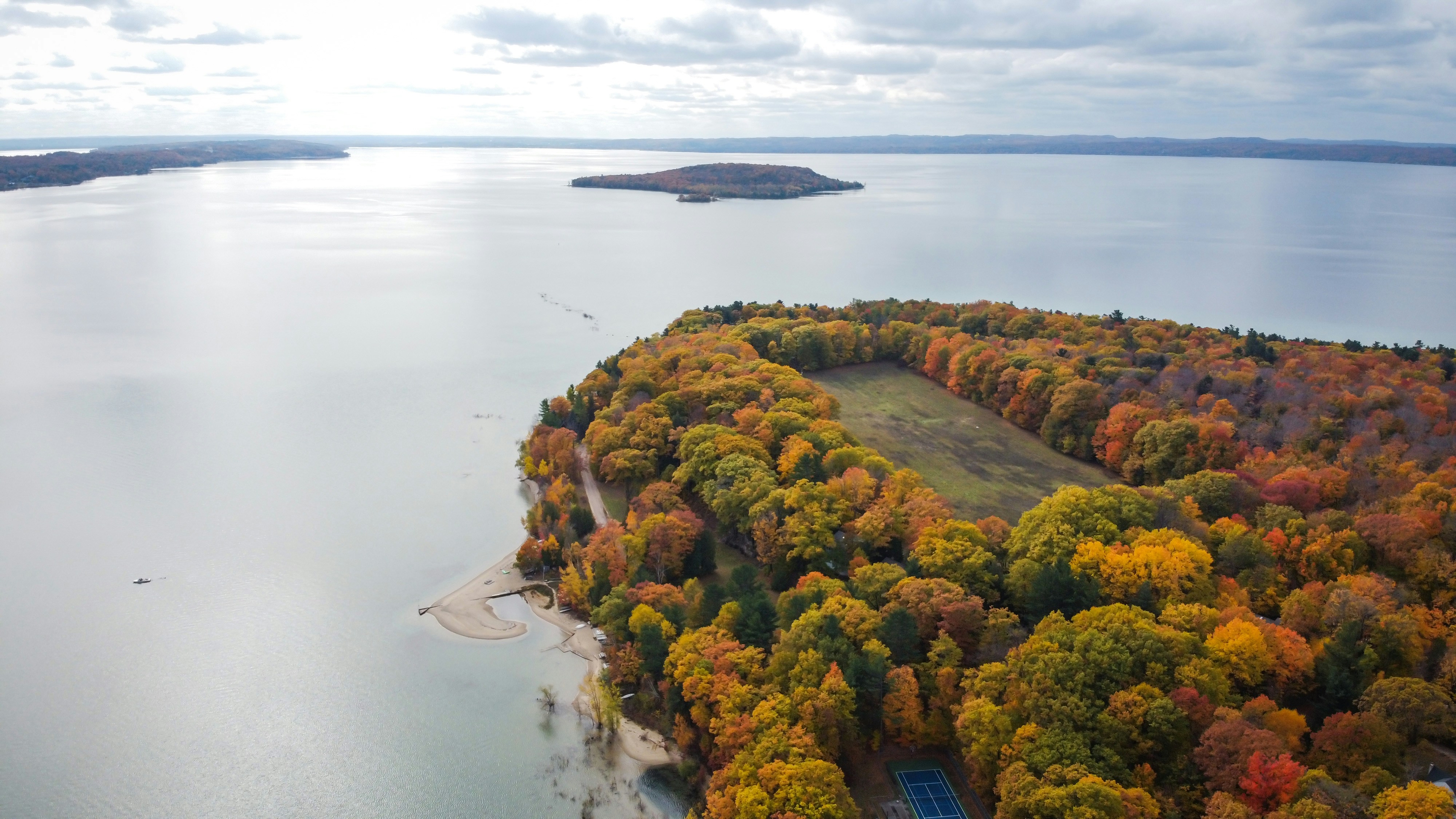 Aerial view of Traverse City, Michigan, with autumn trees, surrounded by a calm lake under a cloudy sky.