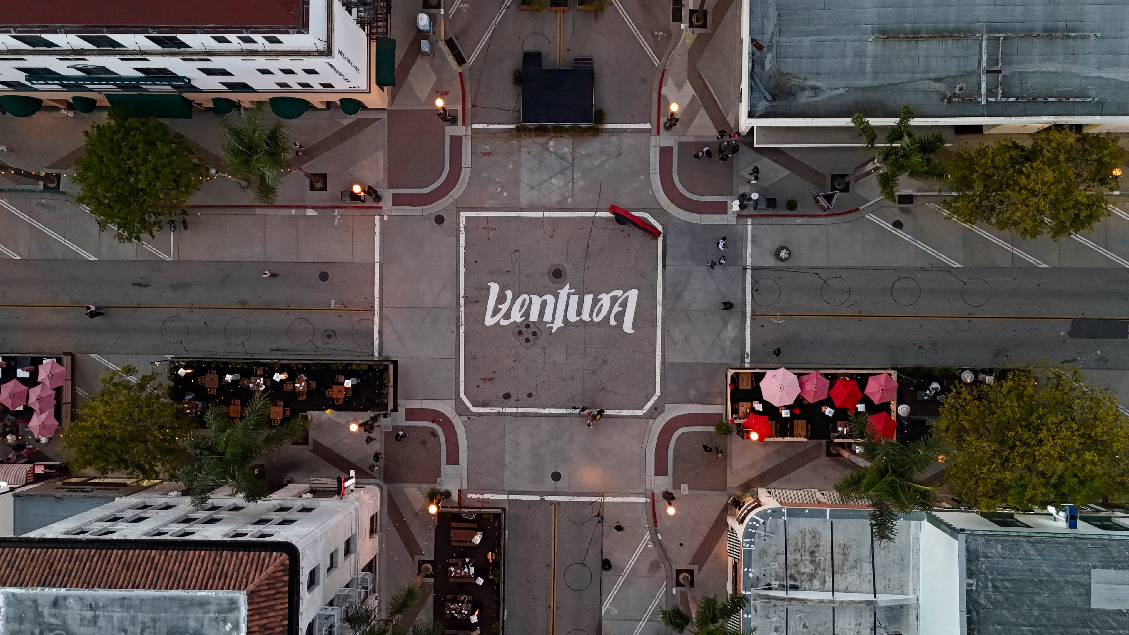 Aerial view of an intersection in Ventura with outdoor dining areas, trees, and buildings. "Ventura" is painted on the street.