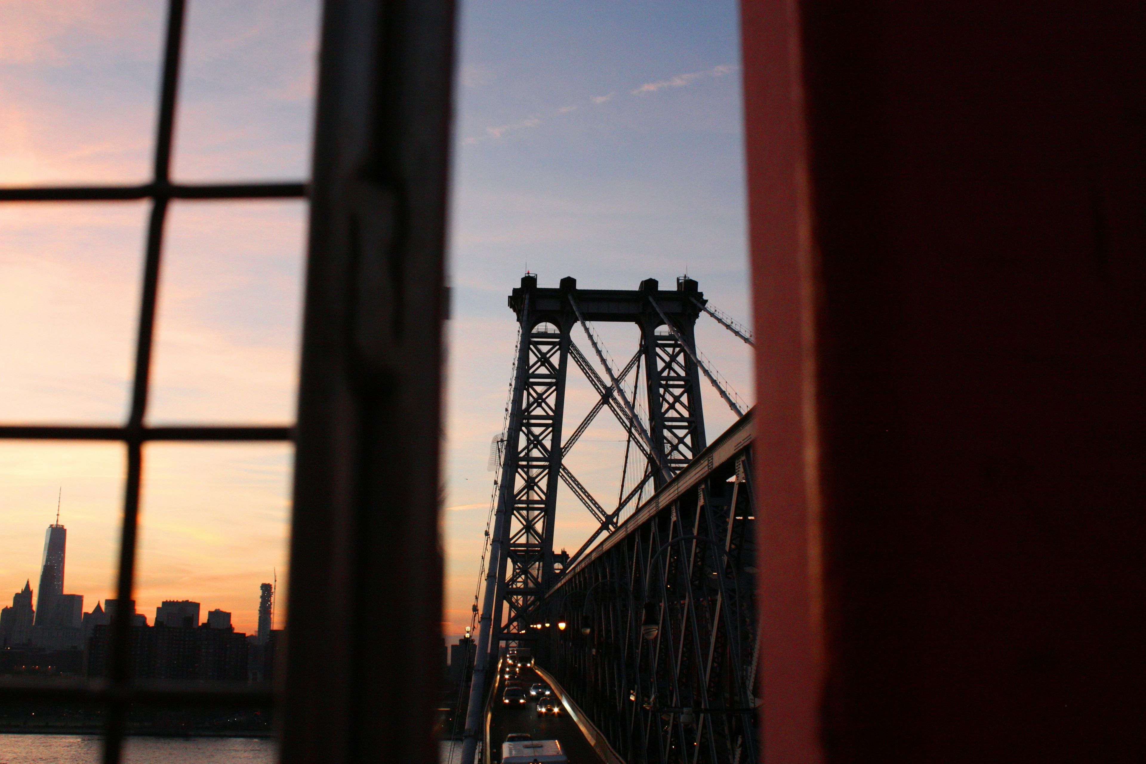 Williamsburg Bridge at sunset with a view of the Manhattan skyline framed between metal railings