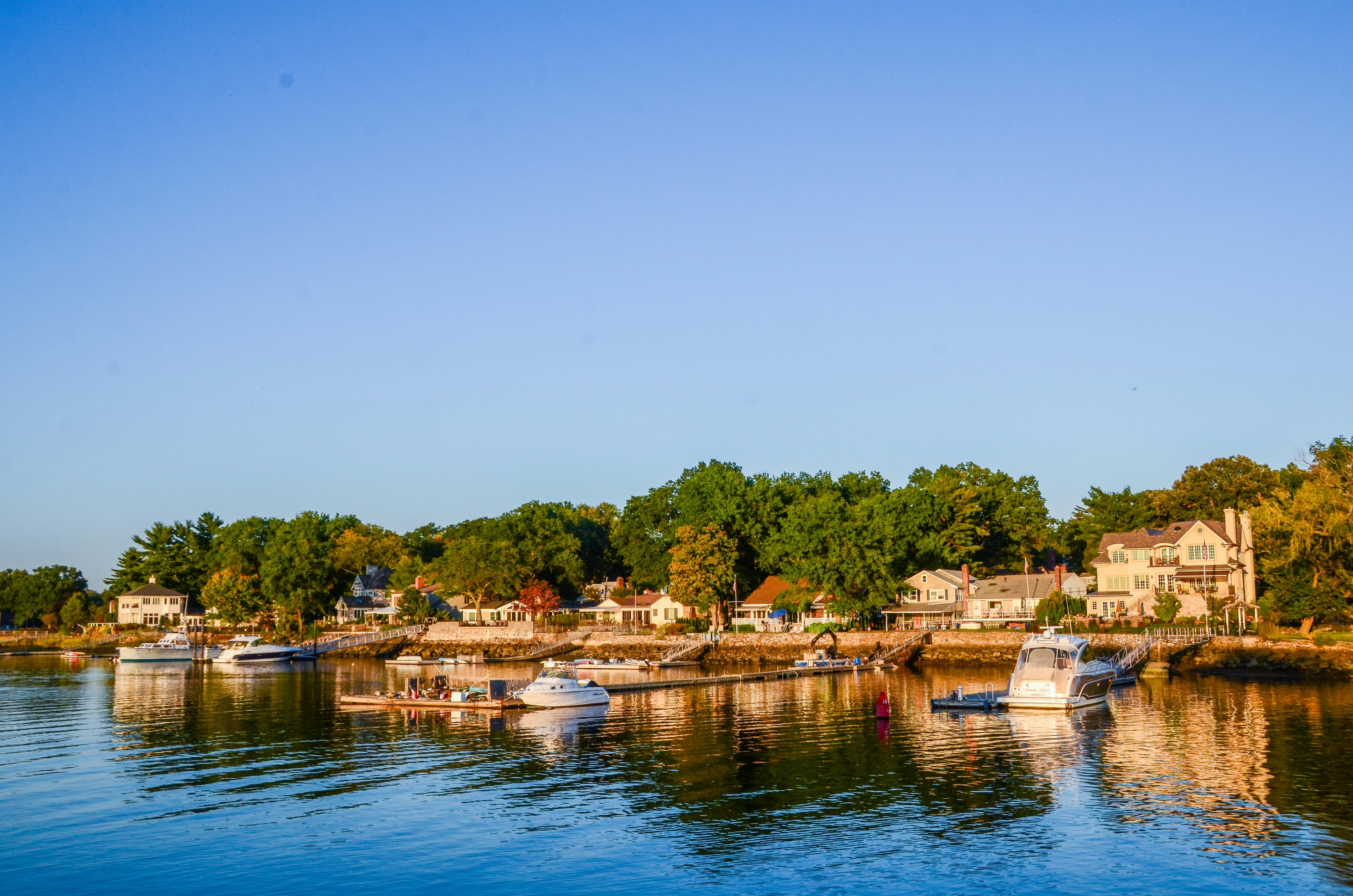 Mamaroneck view with boats docked on calm water, surrounded by lush greenery and houses.