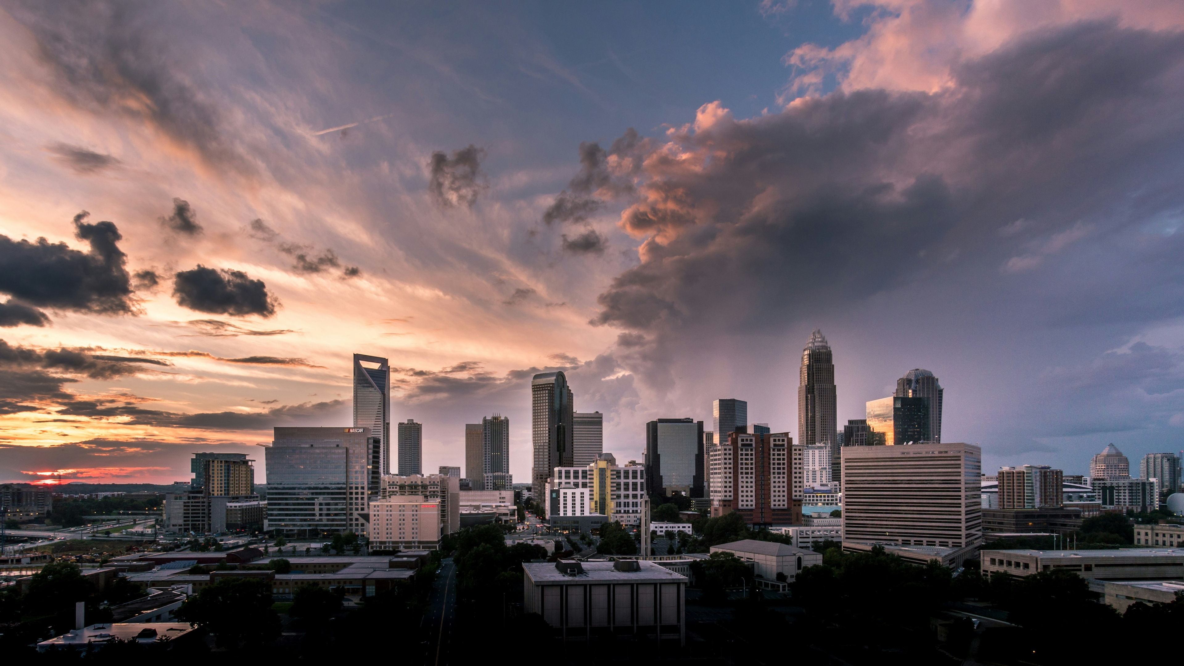 Skyline of Charlotte, North Carolina, at sunset with tall buildings silhouetted against a dramatic sky filled with clouds.