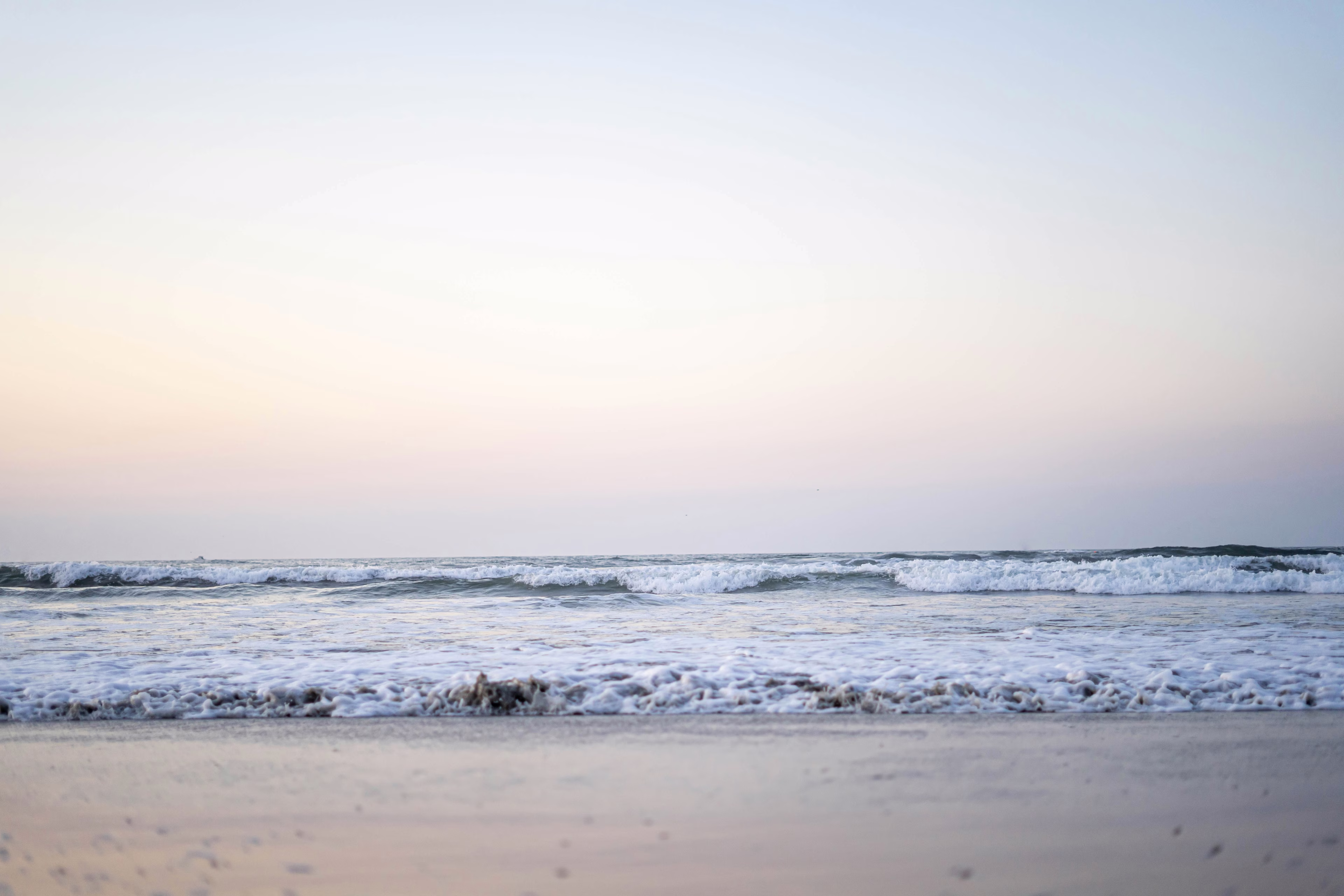 Calm ocean waves gently lapping against the sandy beach in Wildwood, New Jersey, under a pastel-colored sky at dusk