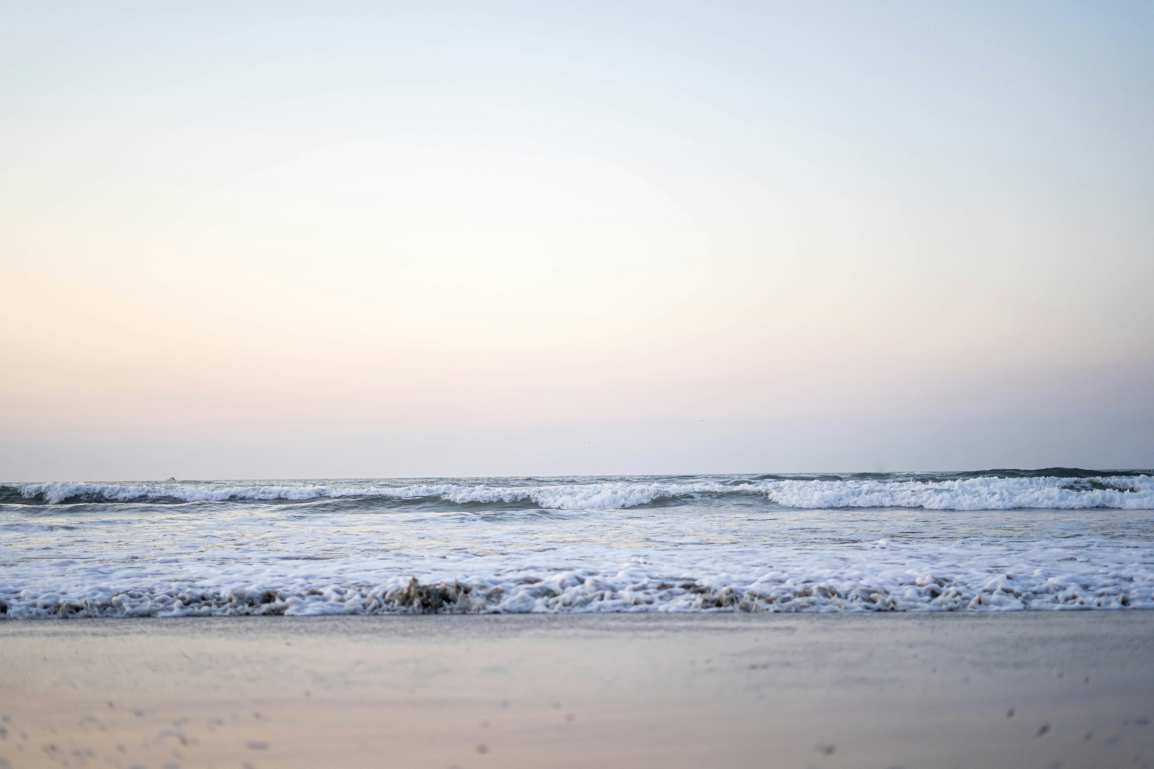 Calm ocean waves gently lapping against the sandy beach in Wildwood, New Jersey, under a pastel-colored sky at dusk