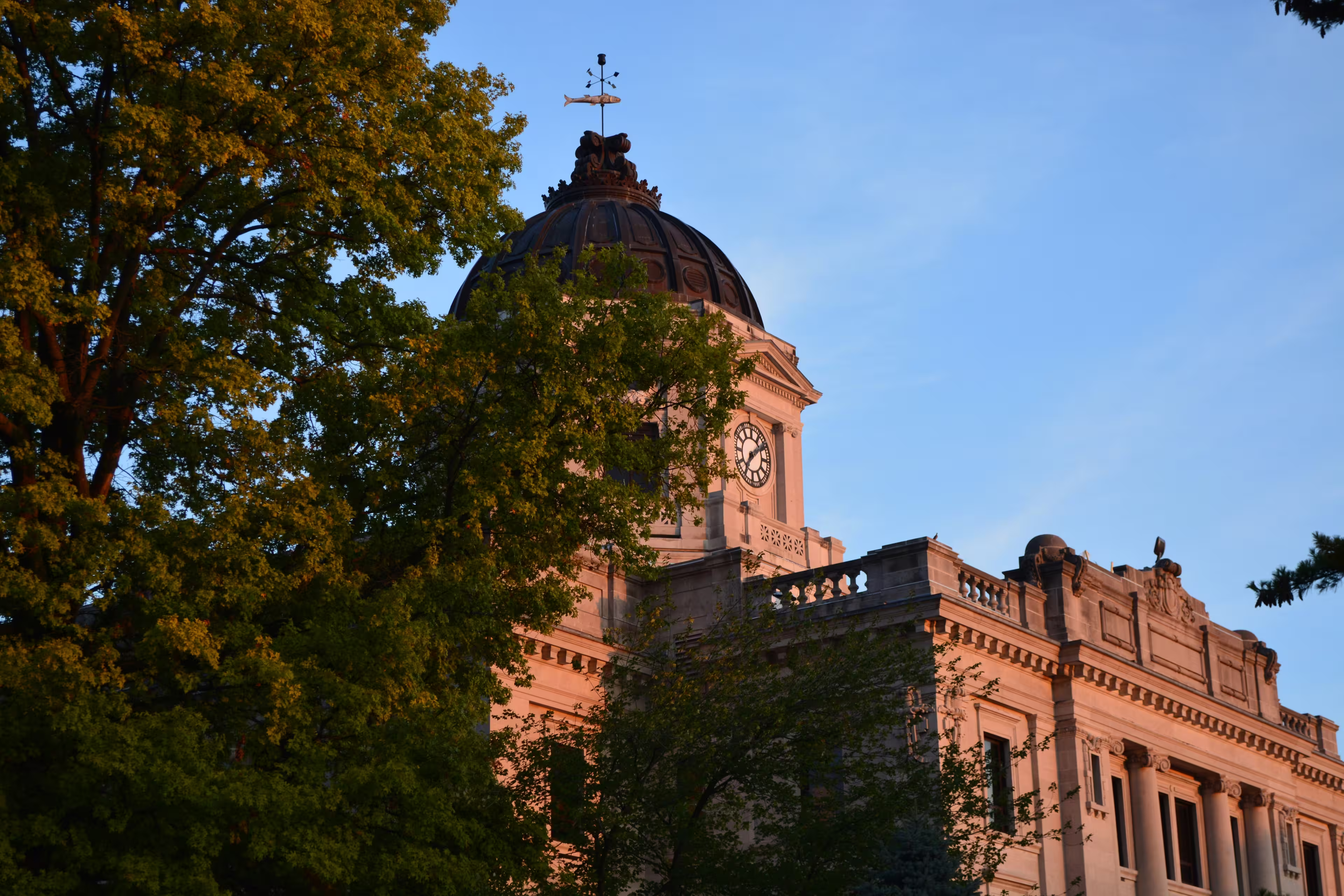 Historic Monroe County Courthouse in Bloomington, Indiana, illuminated by the sunset through surrounding trees.