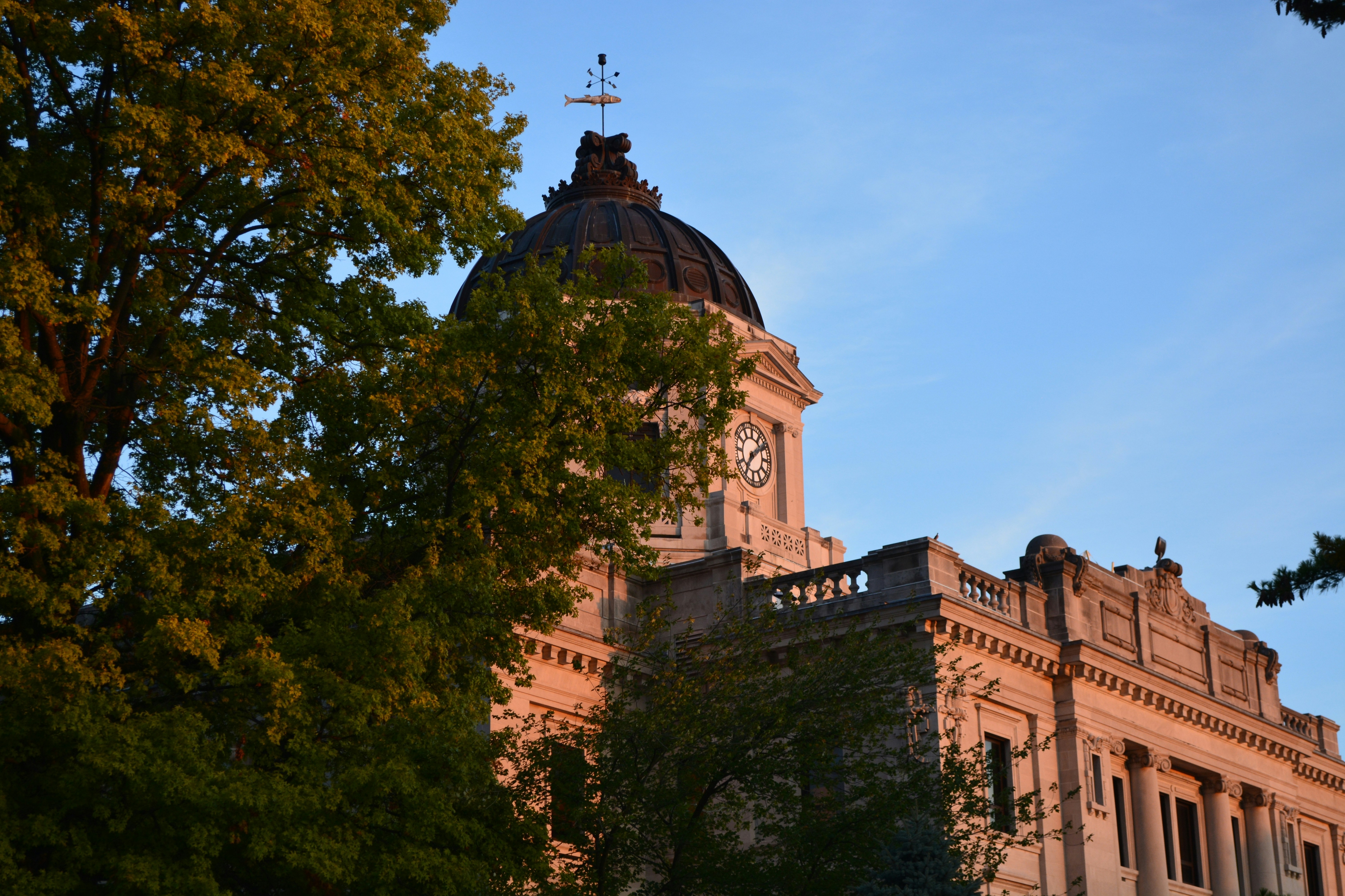 Historic Monroe County Courthouse in Bloomington, Indiana, illuminated by the sunset through surrounding trees.