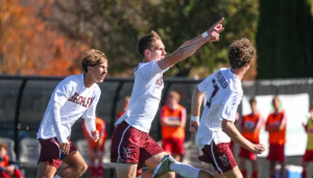 Soccer players in white jerseys celebrate a goal on the field, with one player pointing upward.