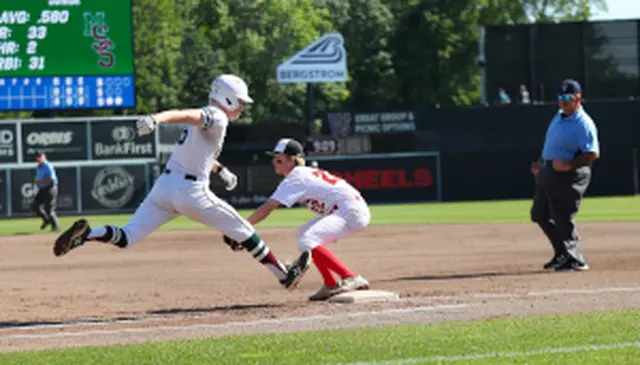 Baseball player in white slides to first base as opponent in red attempts a tag; umpire watches closely.