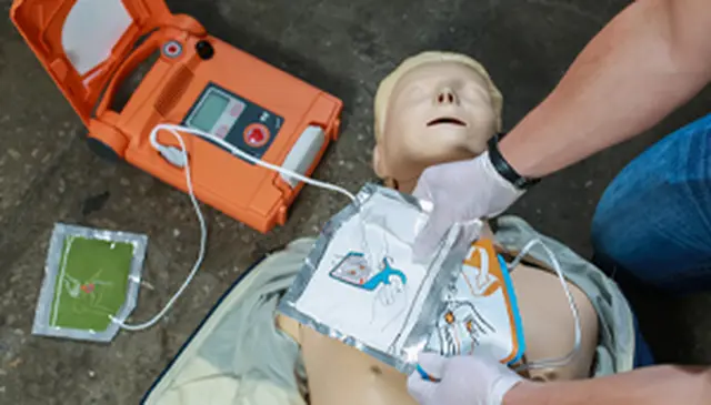Person demonstrating CPR on a mannequin with a defibrillator, attaching electrode pads to the mannequin's chest.