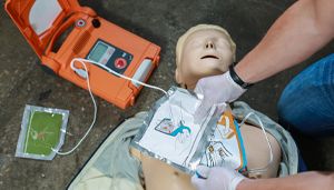 Person demonstrating CPR on a mannequin with a defibrillator, attaching electrode pads to the mannequin's chest.