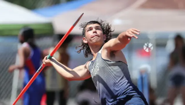 Athlete with long hair in mid-throw, launching a javelin during a track and field event, wearing a sleeveless jersey.