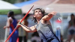 Athlete with long hair in mid-throw, launching a javelin during a track and field event, wearing a sleeveless jersey.
