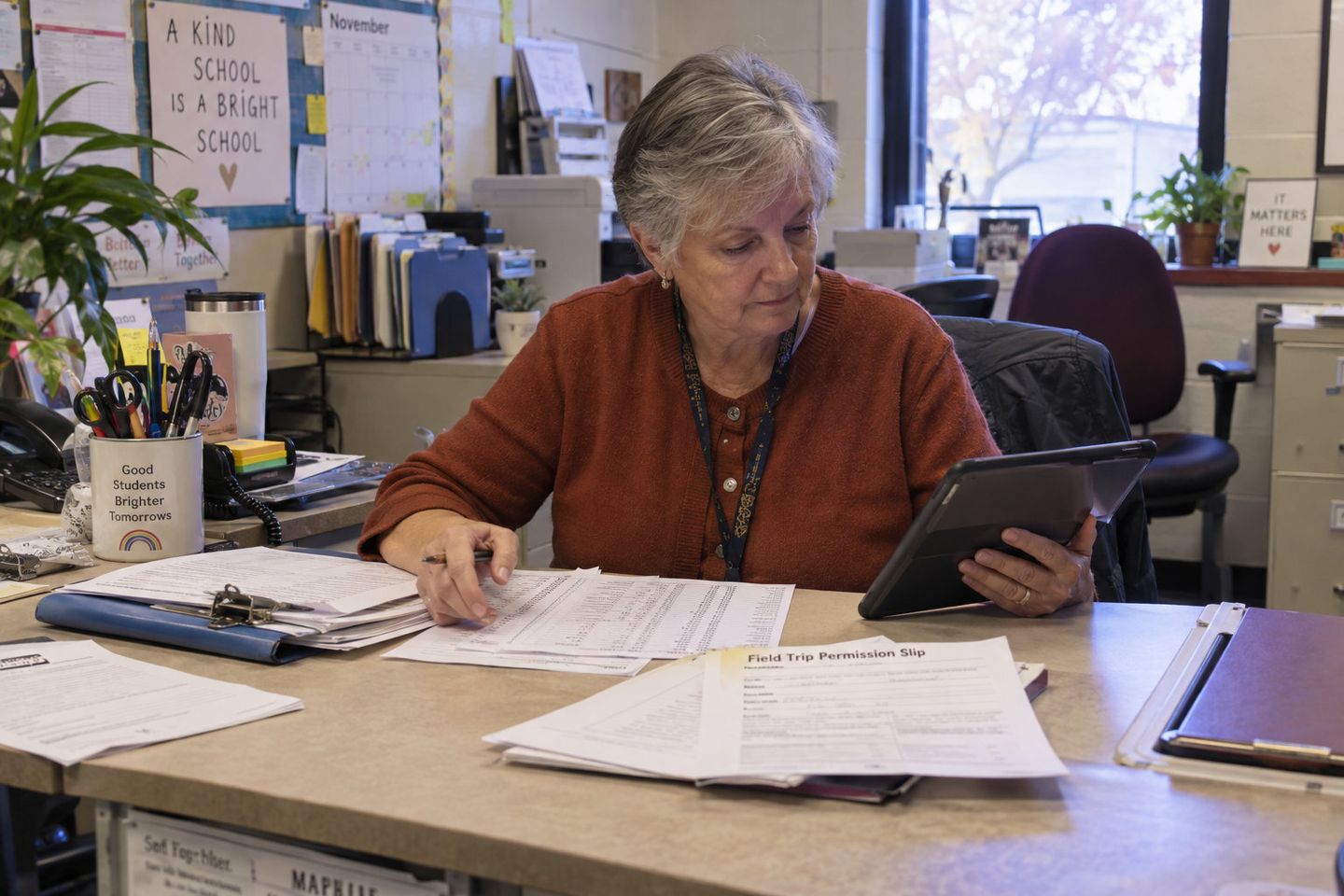 School administrator reviewing paperwork and a tablet at an office desk