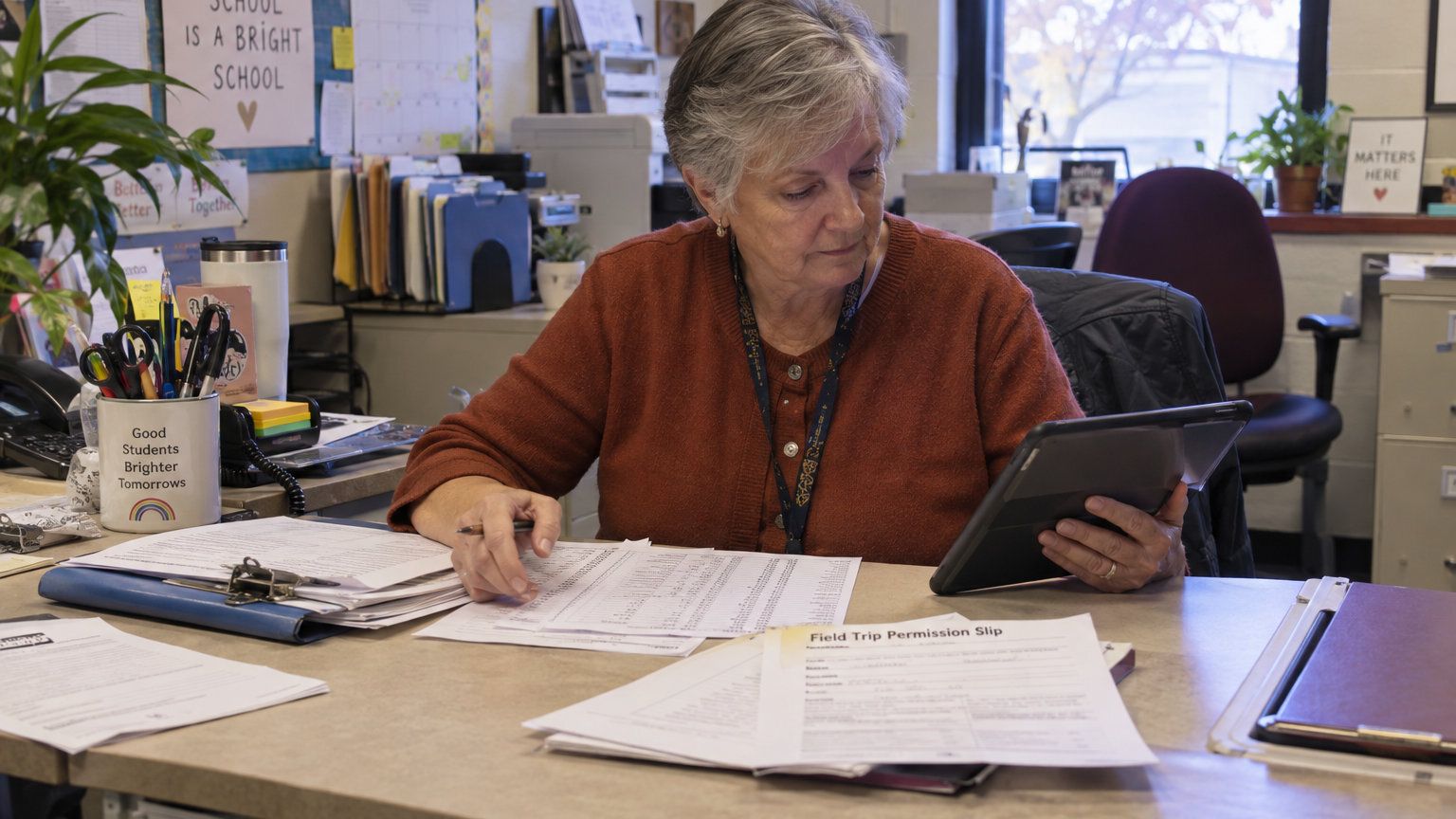 School administrator reviewing paperwork and a tablet at an office desk