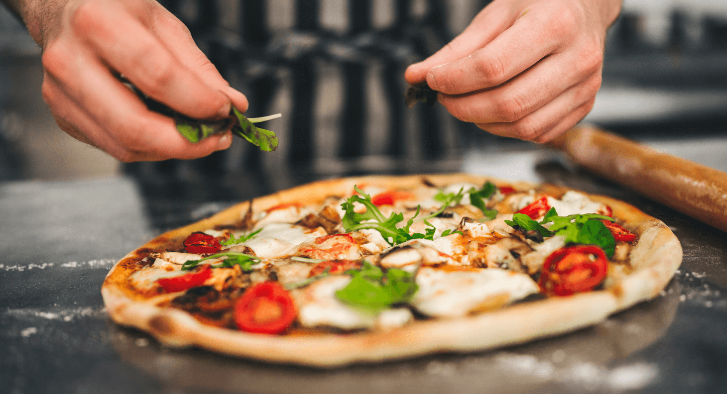 Chef placing spinach and arugula on top of freshly baked pizza with mushrooms and tomatoes
