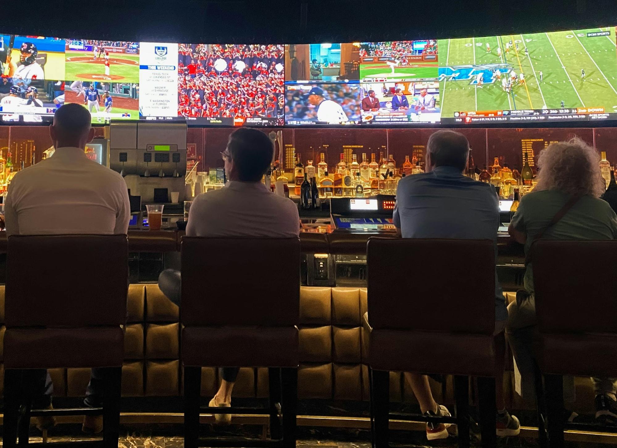 Three men are sitting at a sports bar watching a football game and placing their bets