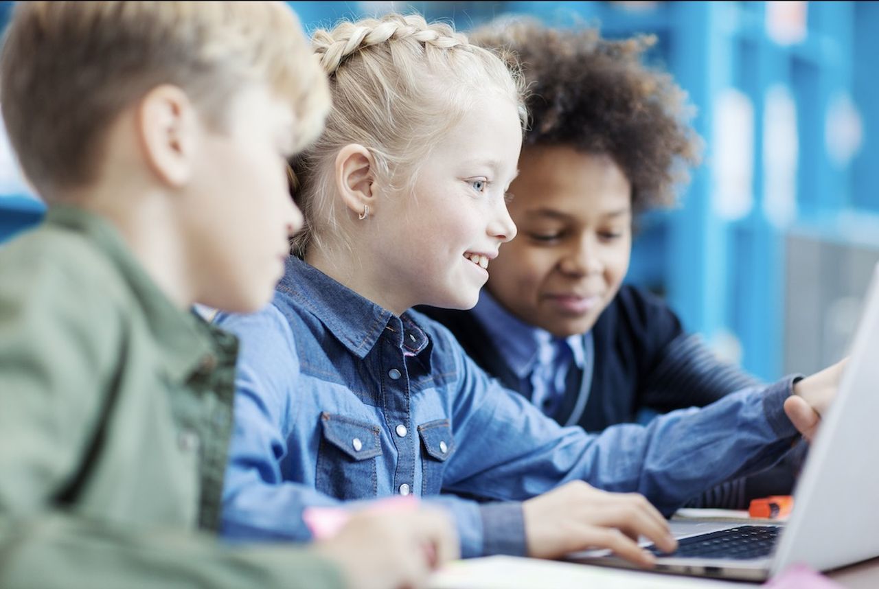 Photo of kids sitting together, focused on a laptop screen