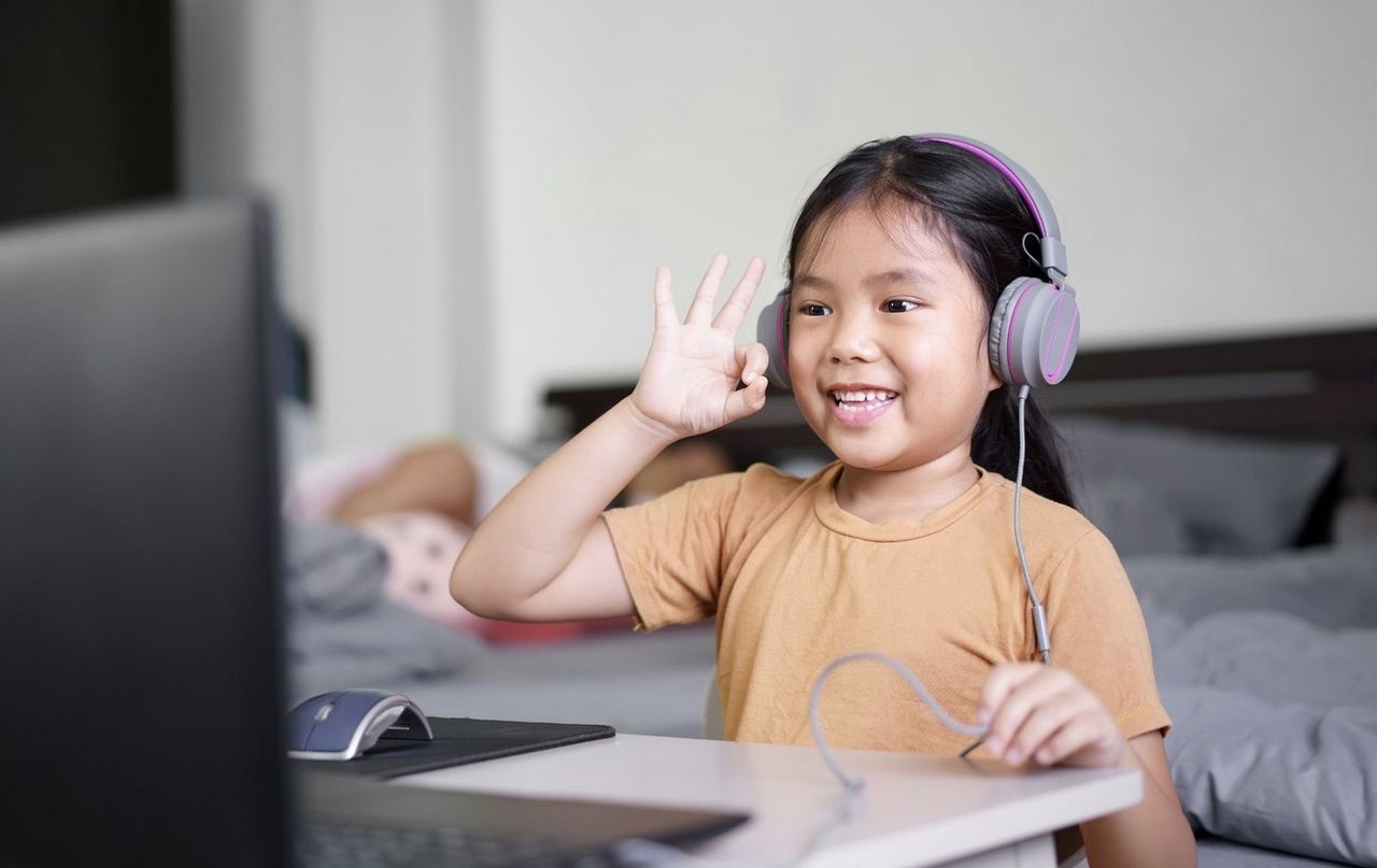 Photo of a girl wearing headphones smiling while sitting in front of a computer desk at home.