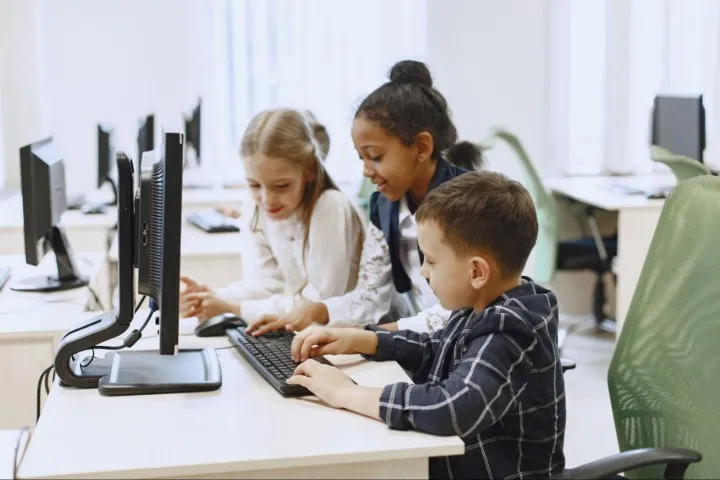 Photo of three kids coding together an a computer in a classroom